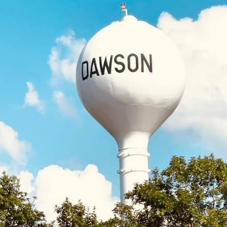 White Dawson, Texas water tower rising above trees against a blue sky with scattered clouds