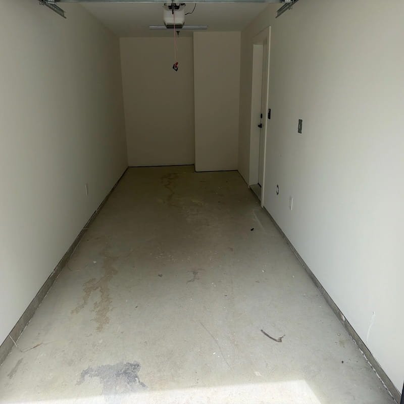 Dusty interior concrete garage floor covered in post-construction debris.