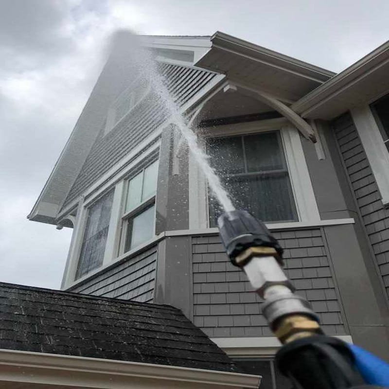 Low-pressure soft wash spray cleaning the exterior siding of a home.