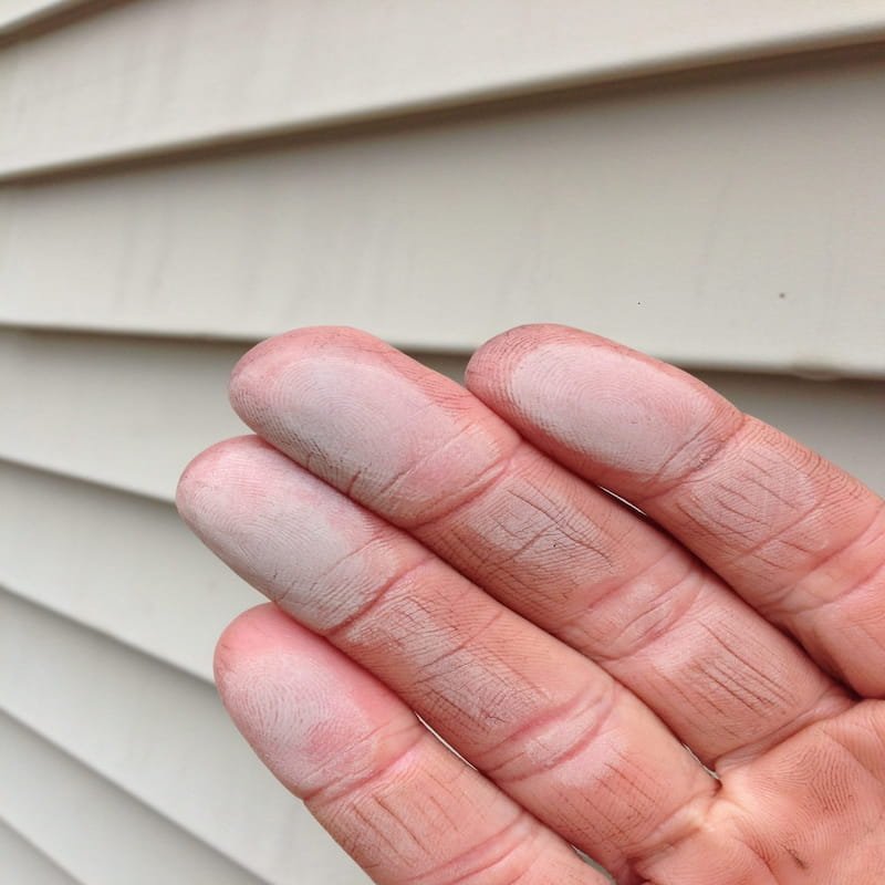 Hand showing white chalky oxidation powder wiped from faded exterior siding.